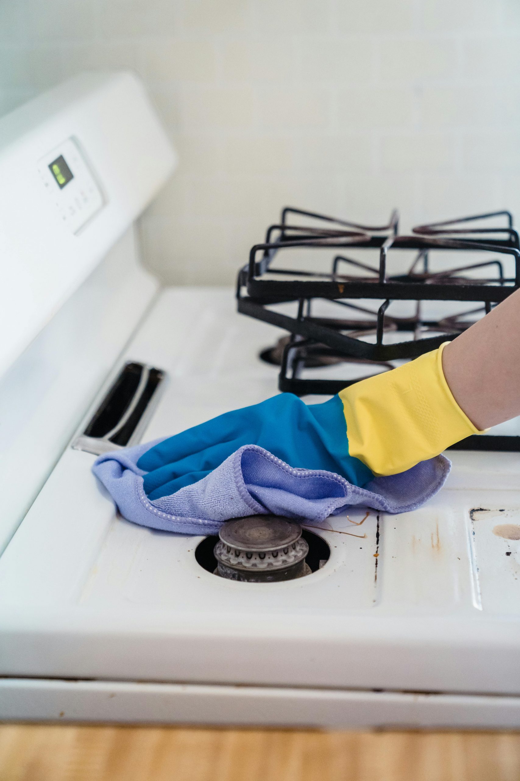 A close-up of a hand in gloves cleaning a gas stove with a cloth.